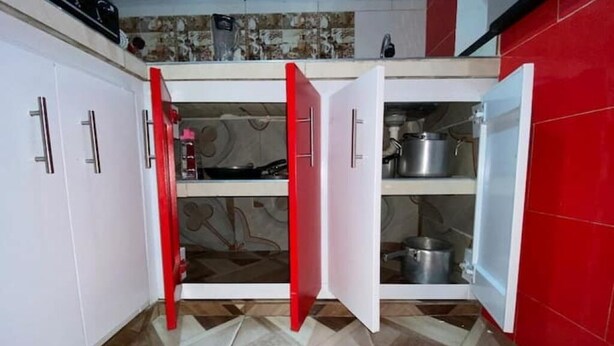 Una cucina con mobili bianchi, una porta rossa e uno schienale piastrellato.