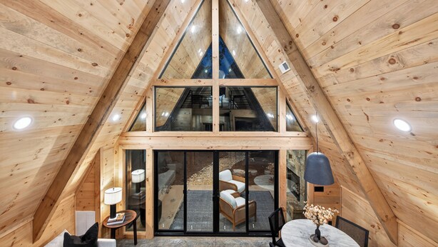 Un intérieur en bois avec un plafond triangulaire, une porte vitrée donnant sur l’extérieur et une table ronde entourée de chaises.