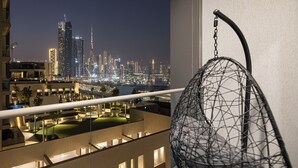 Ein Balkon mit Blick auf eine beleuchtete Skyline bei Nacht, darunter Hochhäuser und ein städtischer Bereich.