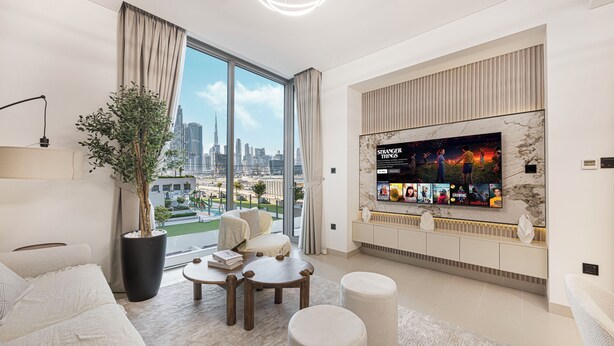 Ein modernes Wohnzimmer mit großem Fernseher, bequemen Sitzmöglichkeiten, einer Topfpflanze und Blick auf eine Stadtlandschaft.