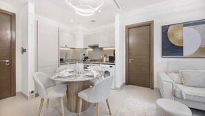 Eine moderne Küche mit integrierten Geräten, eine Essecke mit rundem Tisch und Stühlen sowie ein Wohnbereich mit Sofa und Hocker.