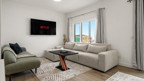 A modern living room with a grey sofa, a green armchair, a black coffee table, and a flat-screen TV mounted on the wall. - Mountain View Retreat with Two King Beds and Full House (Cochrane)