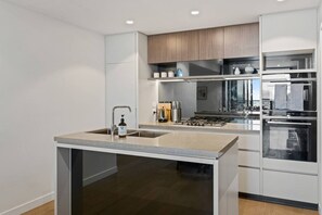 A modern kitchen with a central island, stainless steel appliances, and a wooden upper cabinet. - Luxury 3-Bedroom Stay with City and River View (Brisbane City)