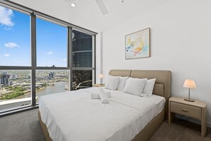 A modern hotel room with a large bed, two bedside tables, a nightstand, a window with a city view, and a painting on the wall. - Luxury 3-Bedroom Stay with City and River View (Brisbane City)