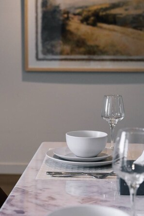 Une table à manger dressée avec des assiettes blanches, un bol, un verre à vin et des couverts.
