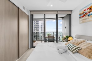 A modern bedroom with a large bed, a view of the city through floor-to-ceiling windows, and a balcony with a table and chairs. - Cozy 1Bedroom Near Casino Luxe Tower&South Bank (Brisbane City)
