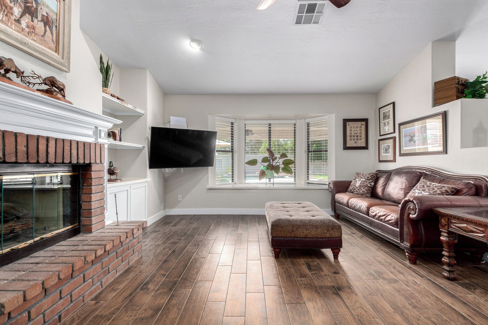 A living room with a fireplace, a flat-screen TV, a leather sofa, and a large window with blinds.