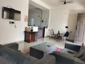 A living room with a TV, a coffee table, and a dining area with chairs. - Family-Friendly 2BHK Homestay with All Amenities (Udaipur)