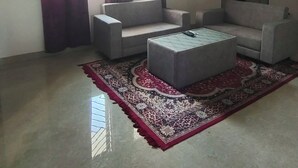 Ein Wohnzimmer mit zwei grauen Sofas, einem zentralen Ottomanen, einem gemusterten Teppich und einem Deckenventilator.