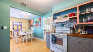 Una cocina con estufa blanca, armarios de madera y un comedor con mesa y sillas blancas.