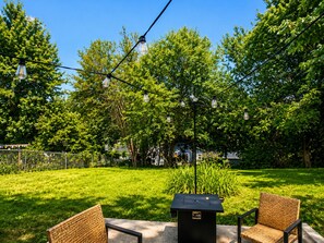 An outdoor seating area with two wicker chairs, a black trash bin, and string lights. - Electric Velvet- 3 bedroom stay near downtown Des Moines (Des Moines)