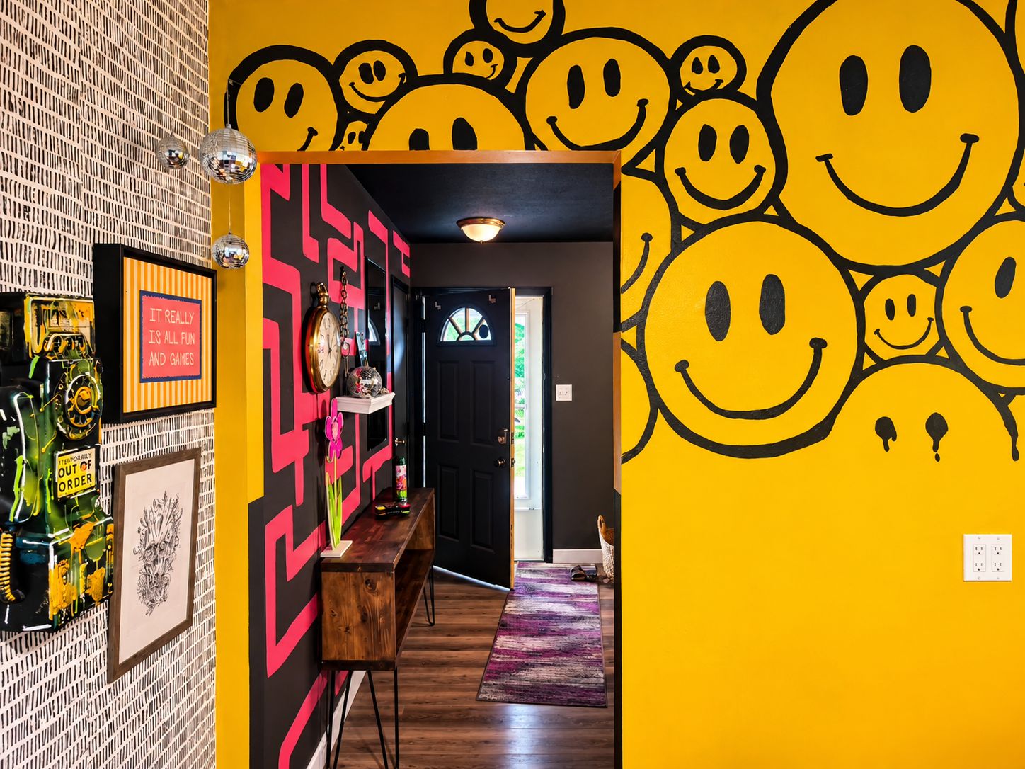 Un pasillo con una pared decorada con caritas sonrientes, un reloj y una estantería con diversos objetos.