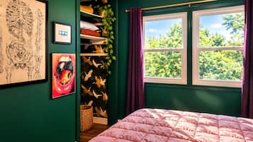 Ein Schlafzimmer mit Bett, Fenster mit Vorhängen und einer grünen Wand mit Kunstwerken.