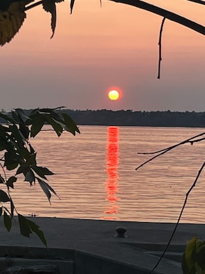 A sunset over a calm body of water with a distant shoreline and a small structure in the foreground.