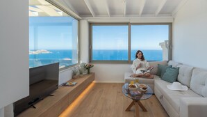 Sala de estar moderna com uma grande janela, televisão de tela plana, sofá, mesa de centro e vista para o mar.