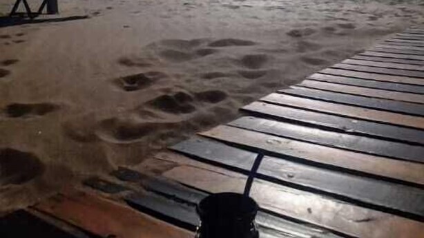 Ein Strand mit einer Holzterrasse, einem Sonnenschirm und Fußabdrücken im Sand.