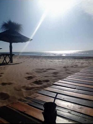 A beach with a wooden deck, a beach umbrella, and footprints in the sand. - Hotel Lincoln (Villa Gesell)