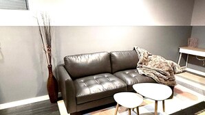 A modern living room with a leather sofa, two small round tables, and a decorative vase. - Family-Friendly 2-Bedroom Unit with Full Bathroom, Living Room, TV & Kitchen (Winnipeg)