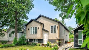 A two-story house with a front yard and a driveway. - Family-Friendly 2-Bedroom Unit with Full Bathroom, Living Room, TV & Kitchen (Winnipeg)
