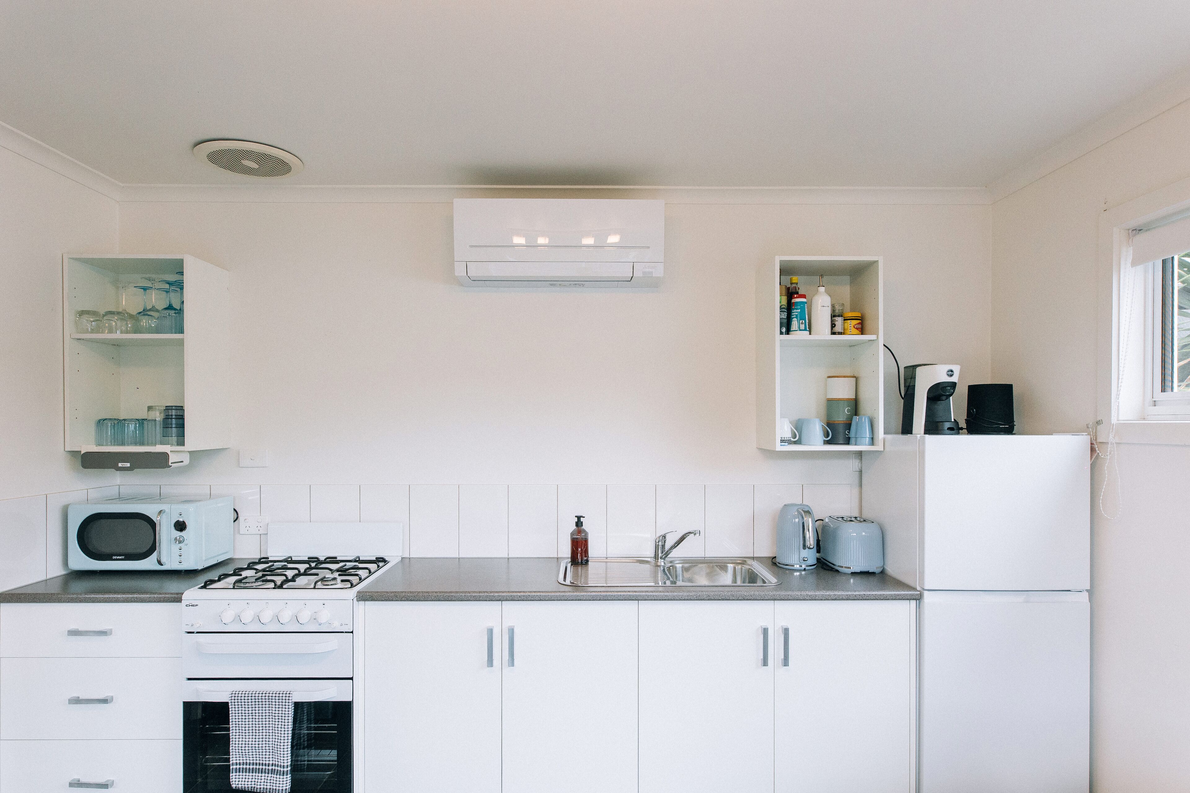 A compact kitchen with white cabinets, a gas stove, a microwave, a sink, and a refrigerator.
