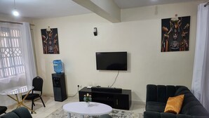 En moderne stue med et fladskærms-tv, sorte sofaer, et rundt sofabord og kunst på væggene.