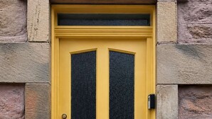 A yellow door with a black glass panel, a mail slot, and a peephole. - The Yellow Door, Inverness (Inverness)