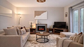 A modern living room with a fireplace, sofa, TV, and a large window. - Ness Gardens, Inverness (Inverness)