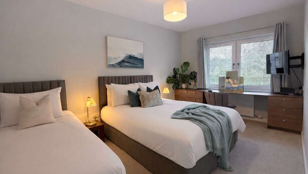 A bedroom with two beds, a desk, a TV, and a window with blinds. - Ness Gardens, Inverness (Inverness)