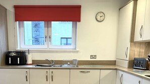 A modern kitchen with white cabinets, a red window blind, a clock, and a toaster. - Ness Gardens, Inverness (Inverness)