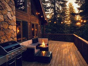 Una terraza de madera con una parrilla, asientos exteriores y un pozo de fuego.