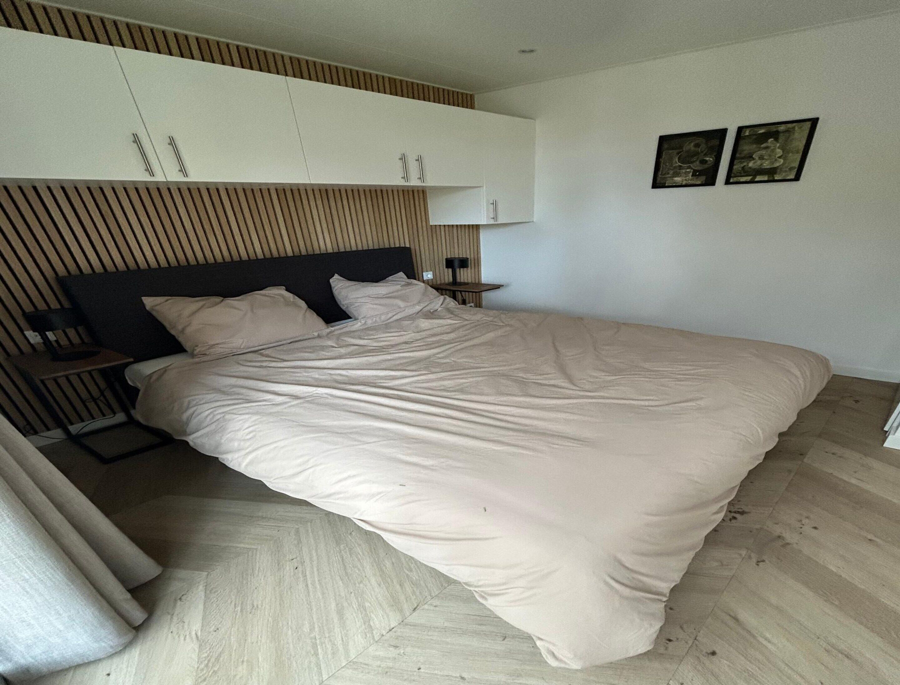 A modern bedroom with a bed, wooden slatted headboard, a nightstand, and two framed pictures on the wall.