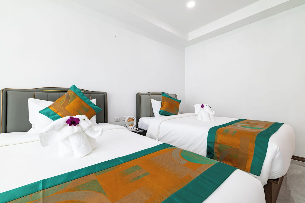 A hotel room with two beds, each with a headboard, white bedding, and orange and green decorative pillows.