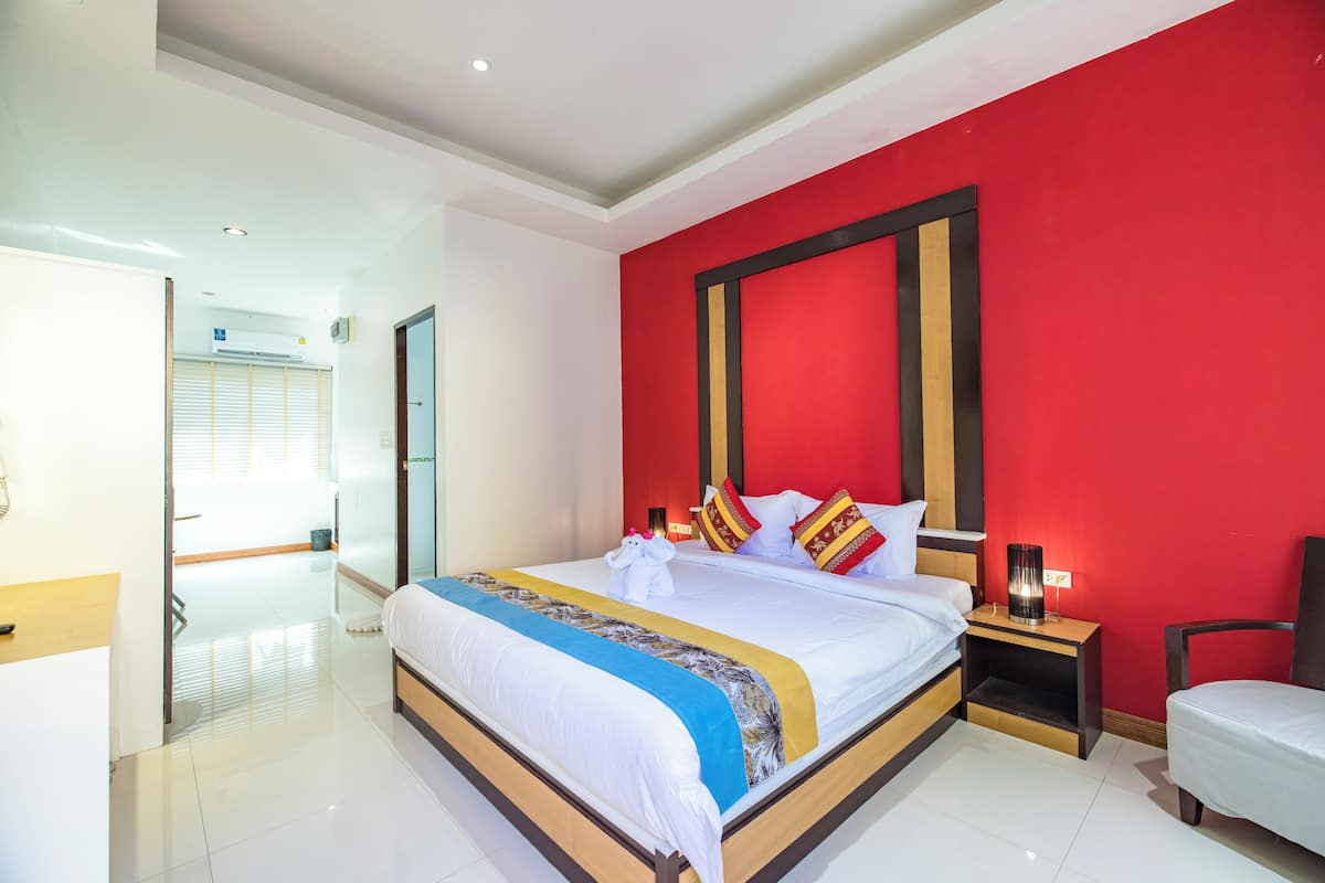 A modern hotel room with a large bed, a bedside table with a lamp, and a red accent wall.