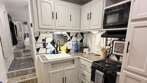 A compact kitchen with white cabinets, a microwave, a stove, and a sink.