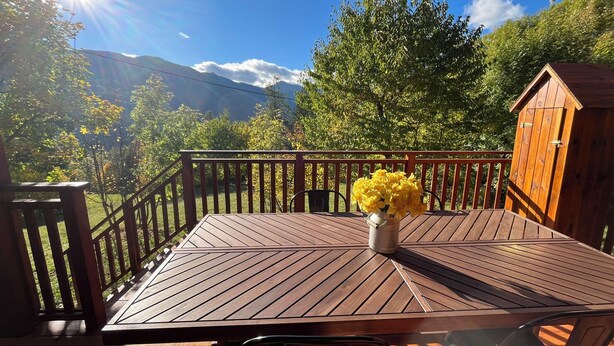 A wooden deck with a table and chairs, a wooden shed, and a mountain view.