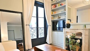A cozy living room with a wooden bench, a sofa, a fireplace, and a bookshelf filled with books. - Élégant 2 chambres au cœur du Marais (Paris)