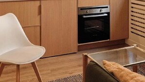 A modern kitchen with wooden cabinets, a black oven, a white chair, and pendant lights. - Elegant Apt near Eiffel Tower, Fast WiFi, (Paris)