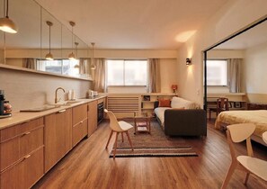 Une chambre d’hôtel moderne et compacte, dotée d’une kitchenette, d’un canapé, d’un lit et d’un coin repas.