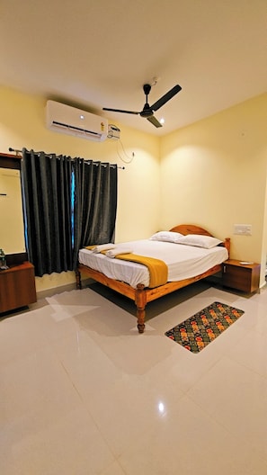 Quarto de hotel com cama, ventoinha no teto, ar condicionado, mesa de cabeceira e tapete estampado.