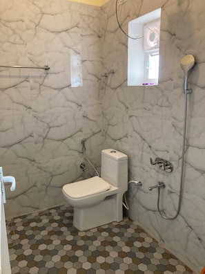A bathroom with a toilet, a shower, and a small window. - Leela Sea Scape (Kumta)