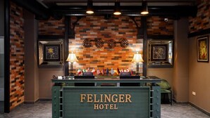 Een receptiebalie met de tekst 'FELINGER HOTEL' en een muur met klokken en vlaggen.