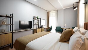 Een moderne hotelkamer met een groot bed, een bureau met een computer, een televisie en een zithoekje met stoelen.