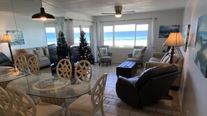 A spacious living room with a glass dining table, comfortable seating, a Christmas tree, and a view of the ocean. - AMI Bridgeport 202 -Beach View Retreat+Resort Pool (Bradenton Beach)