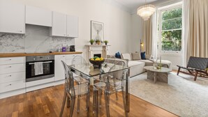 Una cocina moderna con armarios blancos, encimera de mármol y mesa de comedor de vidrio.