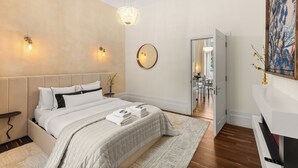 Un dormitorio moderno con una cama grande, lámparas de noche, un espejo redondo y un cuadro en la pared.