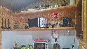 A kitchen with wooden shelves, a microwave, a toaster, a kettle, and a sink. - Acorn corner in a wooden house (Leiria)