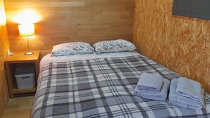 A cozy room with a plaid bedspread, two pillows, a bedside lamp, and neatly folded towels on the bed. - Acorn corner in a wooden house (Leiria)