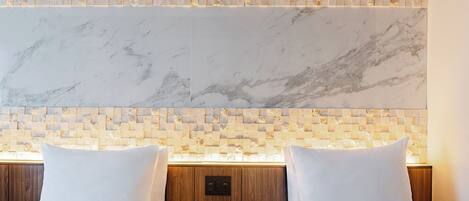 Habitación de hotel con dos camas, cabecera de mármol y pared de mosaico.