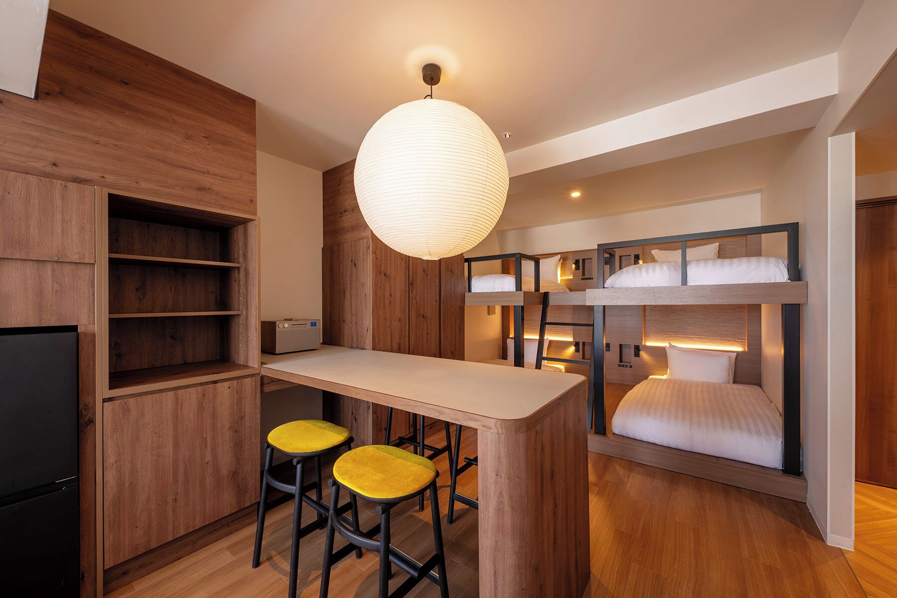 A compact, modern kitchen with wooden cabinetry, a central island with stools, and a hanging light fixture.