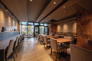 A modern restaurant interior with a bar area, seating arrangements, and large windows providing natural light.